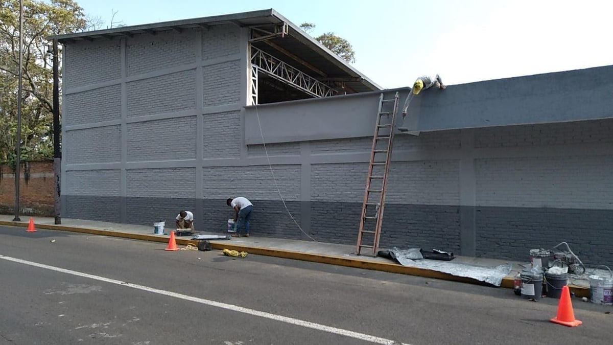 Construction workers on ladder and ground working on large gray commercial building exterior with metal beam framework visible