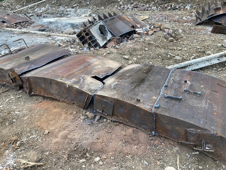 Rusted metal vehicle parts and debris scattered on rocky ground at an auto salvage or scrapyard