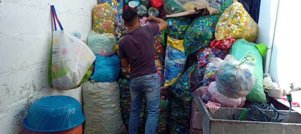Person organizing colorful plastic bags and waste materials in a cluttered storage space or recycling area
