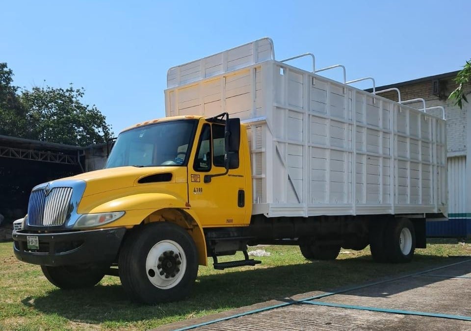 Yellow International truck with large white metal cargo bed parked on grass with clear blue sky background